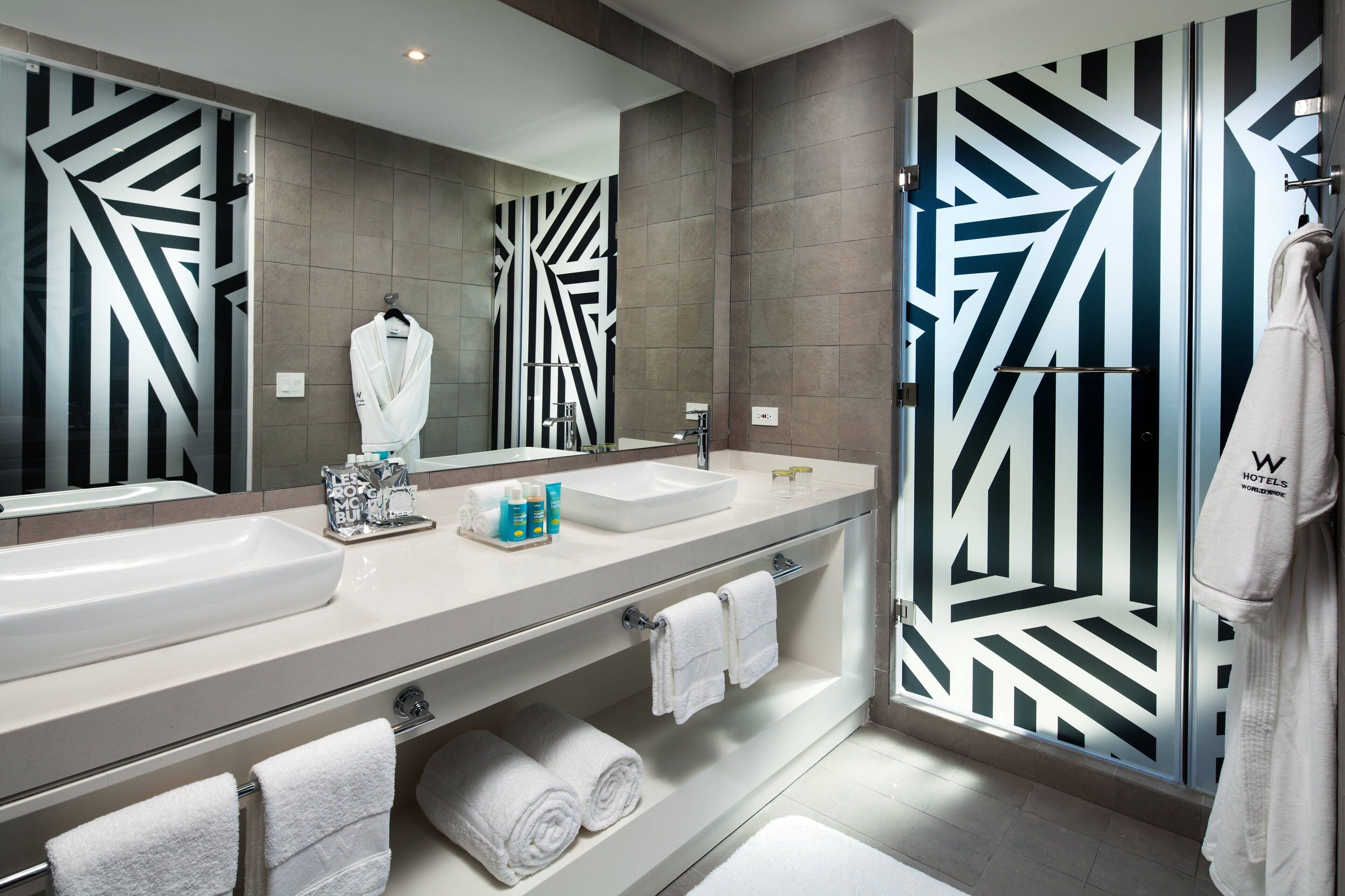 Une salle de bain moderne avec un grand miroir, deux lavabos et un espace douche.