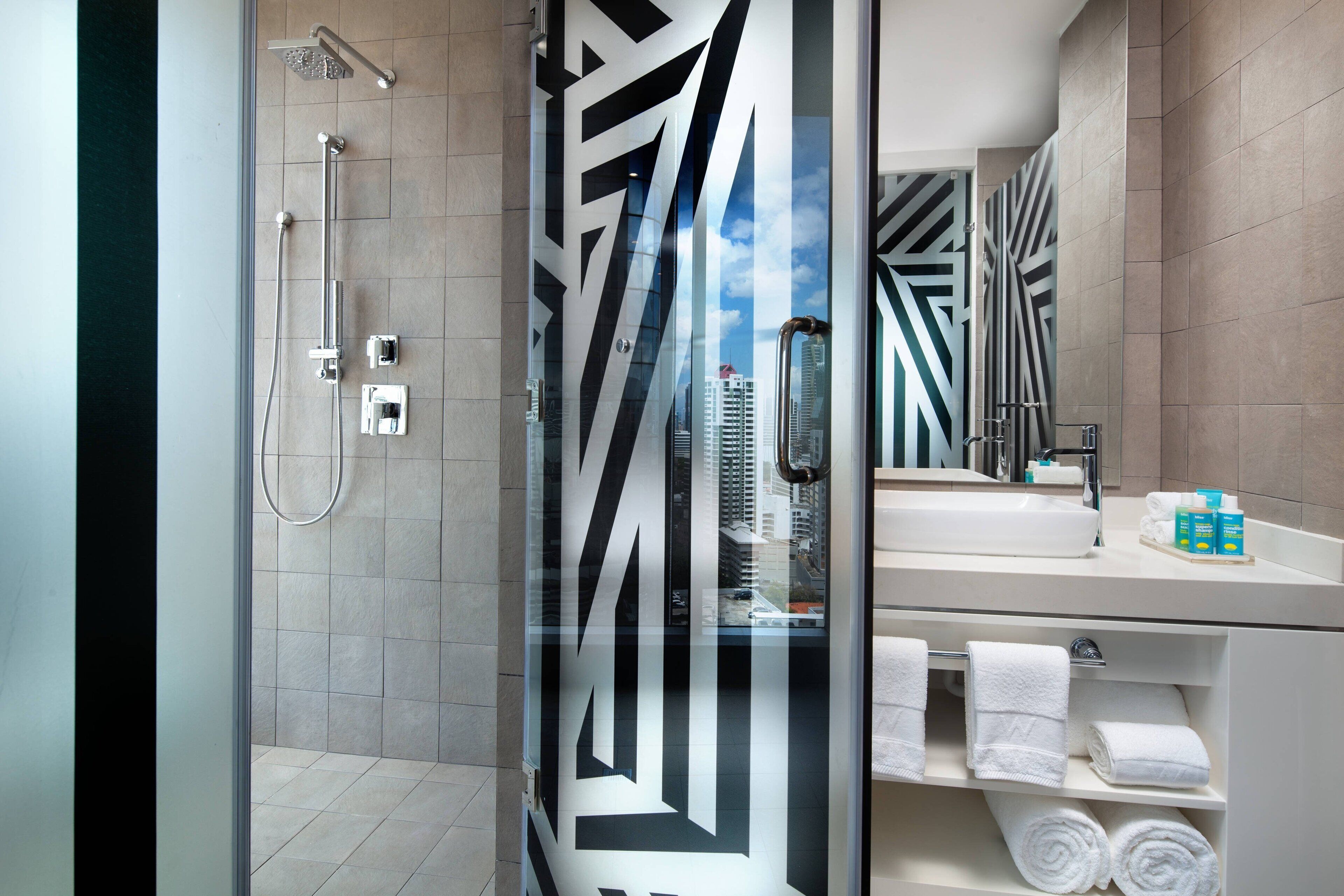 Une salle de bain moderne avec une douche à parois de verre, un grand miroir et un meuble-lavabo avec des articles de toilette.