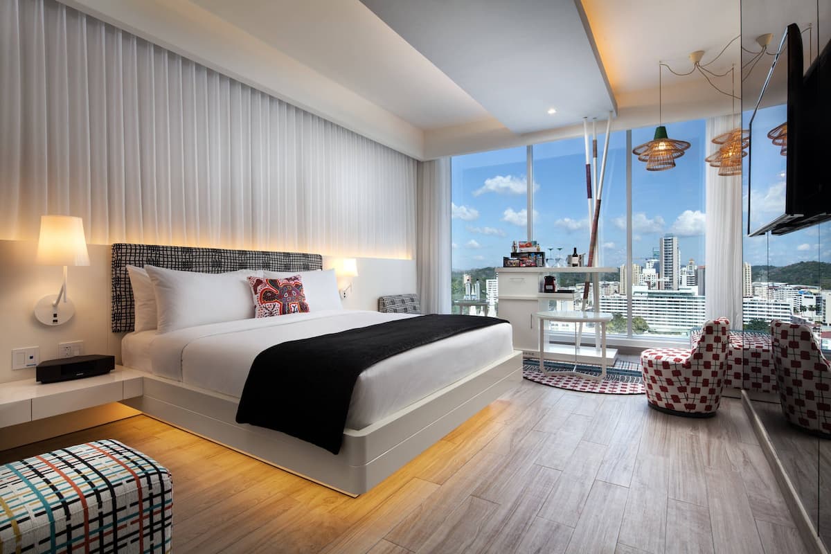Habitació d'hotel moderna amb un llit gran, vistes a la ciutat i un balcó amb seients.