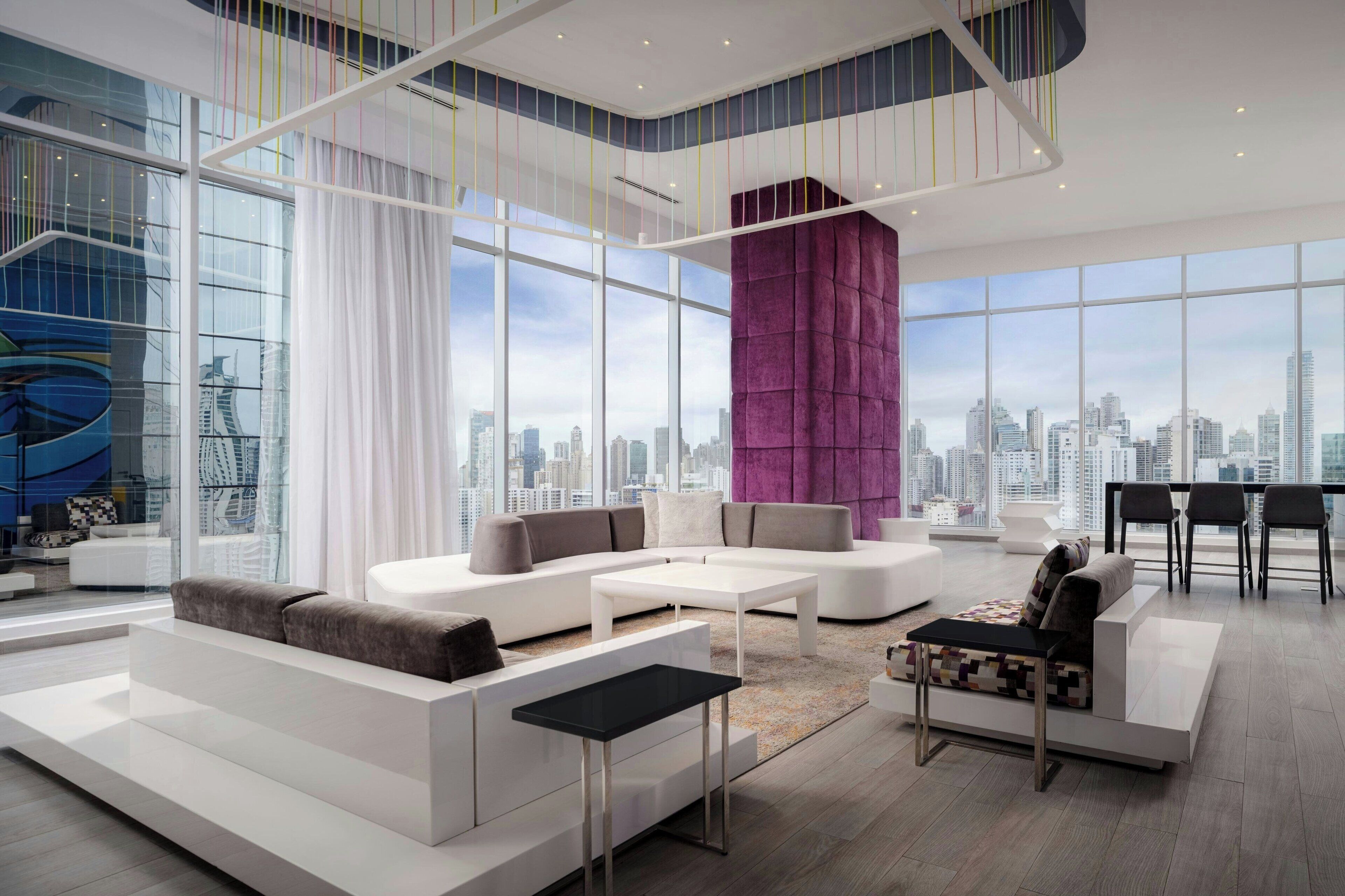 A modern living room with a city view, white sofas, a coffee table, and a purple accent wall.