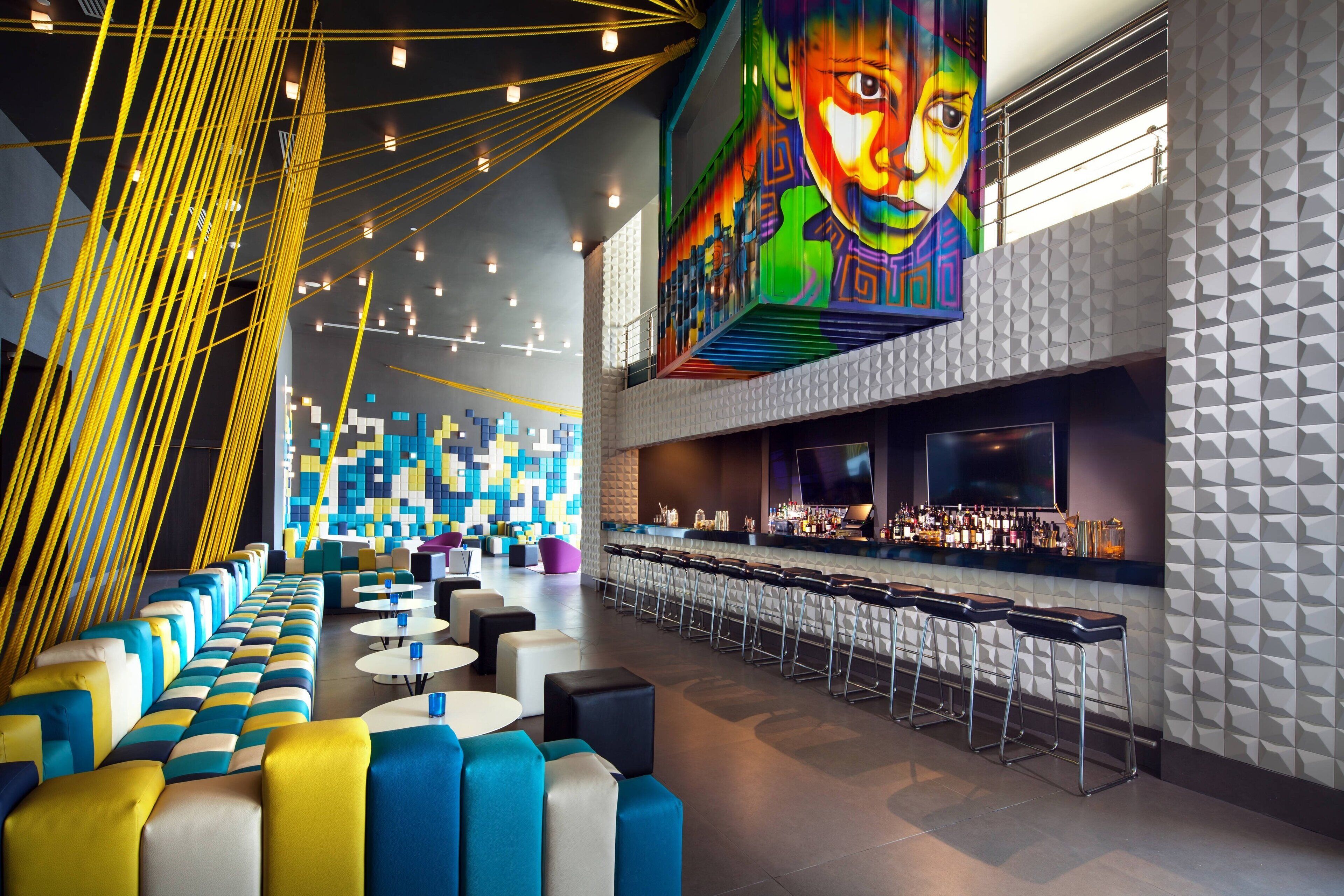 A modern bar area with a long counter, multiple stools, and a colorful mural on the wall.