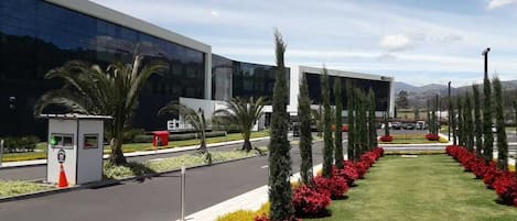 A modern building with a reflective glass facade, a well-maintained lawn with colorful flower beds, and a clear sky.