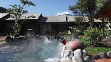 A hot spring area with a stone pathway, a traditional building, and a mountain in the background.