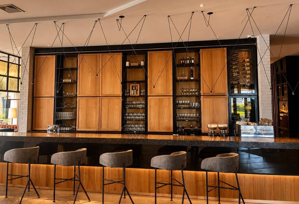 Una zona de bar con armarios de madera, taburetes y lámparas colgantes.