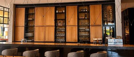 A bar area with wooden cabinets, bar stools, and hanging light fixtures.