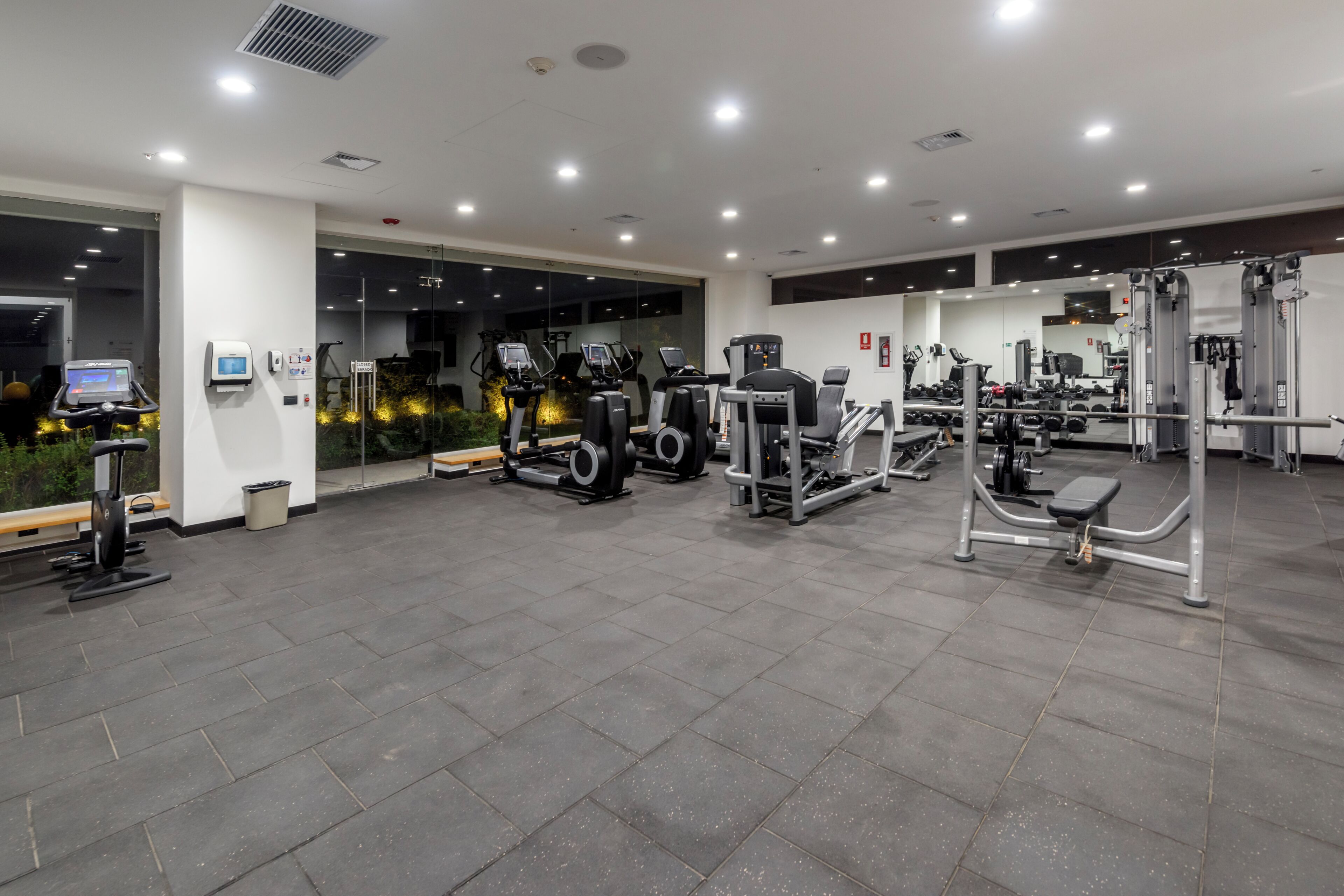 A gym with various exercise equipment, including treadmills and weight machines, and a digital display.