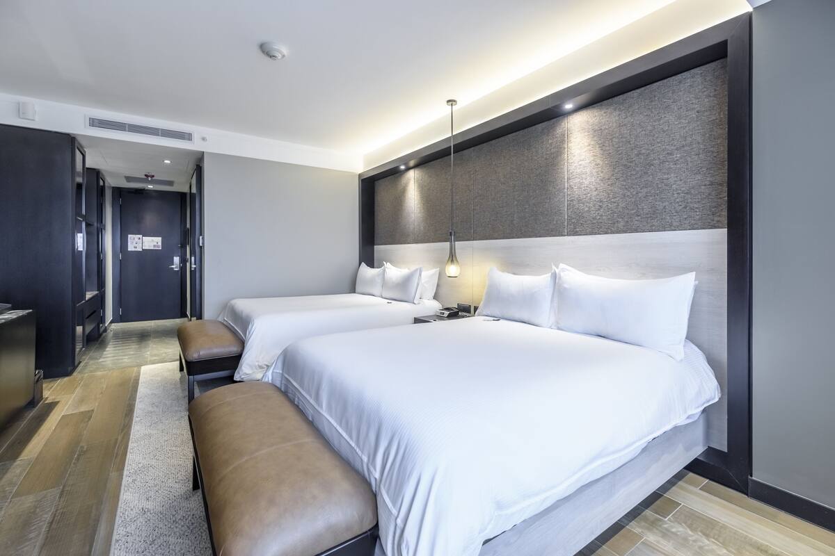 Una habitación de hotel moderna con dos camas, un banco, un escritorio y un panel grande en la pared.