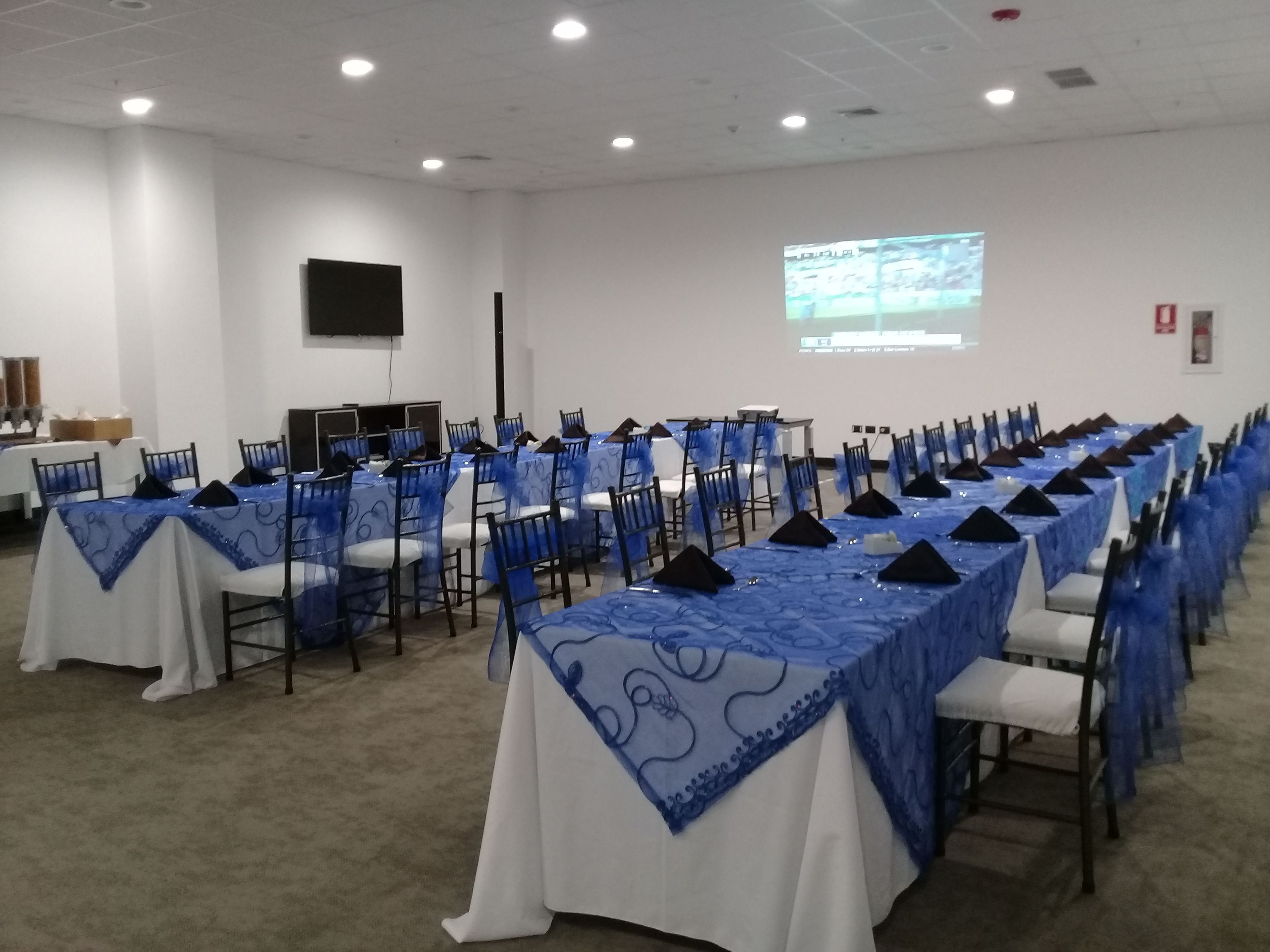 Un salón de conferencias con mesas y sillas en filas, una pantalla de proyector y una pizarra.