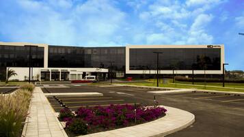 A modern hotel with a glass facade, a parking lot, and landscaped flower beds.