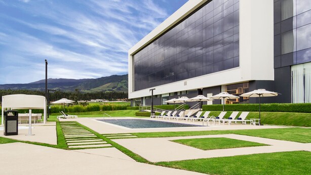 Un edificio moderno con piscina, sillones de descanso y una zona cubierta.