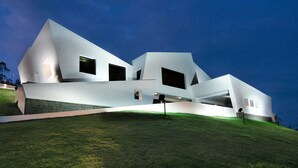 Un edificio moderno de varios niveles, blanco, con techo inclinado, ventanas amplias y un paisaje cubierto de césped.