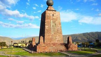 A tall brick monument with a spherical top, surrounded by a landscaped area with pathways and a view of distant hills.