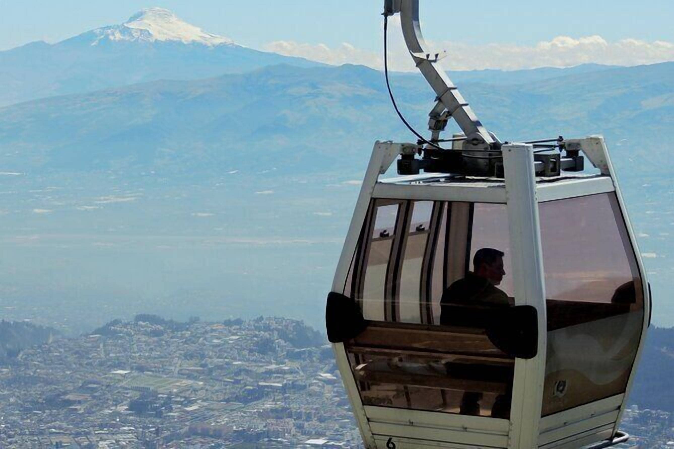 A cable car with a passenger, offering a view of a city and a mountain in the background.