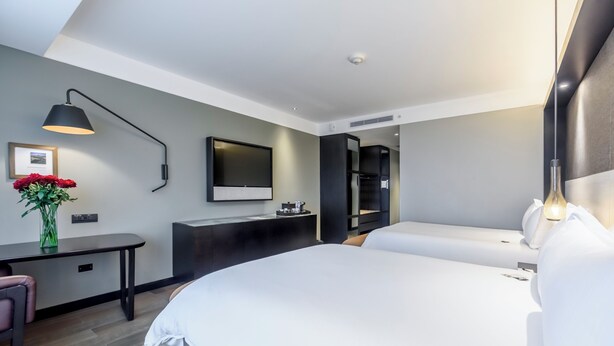 A modern hotel room with a large bed, a desk, a chair, a TV, and a mirror.