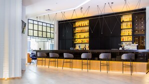 Un área de bar moderna con una barra larga, varios taburetes y estantes llenos de botellas.