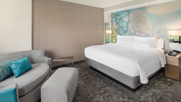 Ein Hotelzimmer mit einem großen Bett, einem grauen Sofa, einem kleinen Tisch und einer Wand mit einer strukturierten Wandmalerei.