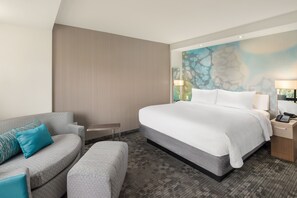 A hotel room with a large bed, a grey sofa, a small table, and a wall with a textured mural. - Courtyard by Marriott Albion (Albion)