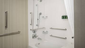 A modern bathroom with a bathtub, shower, and toilet. It includes grab bars and a shelf with toiletries.