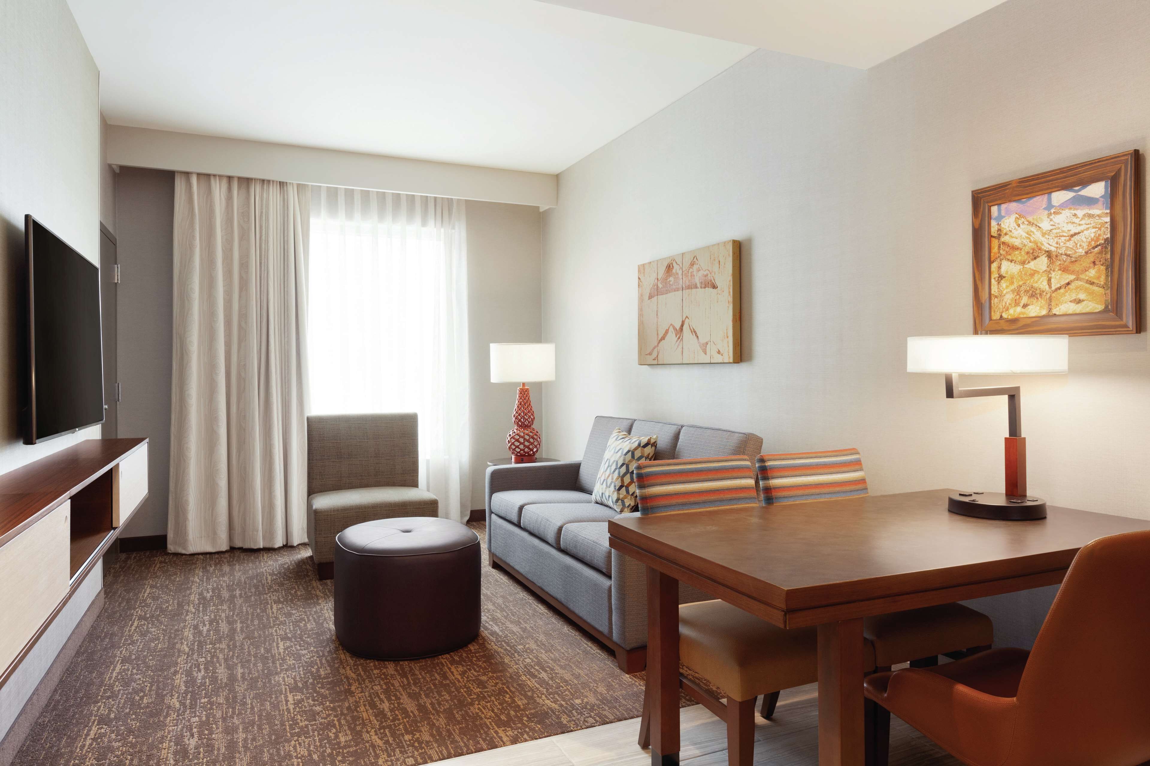 Habitación de hotel con televisión de pantalla plana, sofá, mesa de comedor y lámpara.