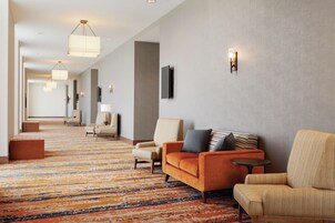 Un hall de hotel con alfombra estampada, varias zonas de estar e iluminación colgante.
