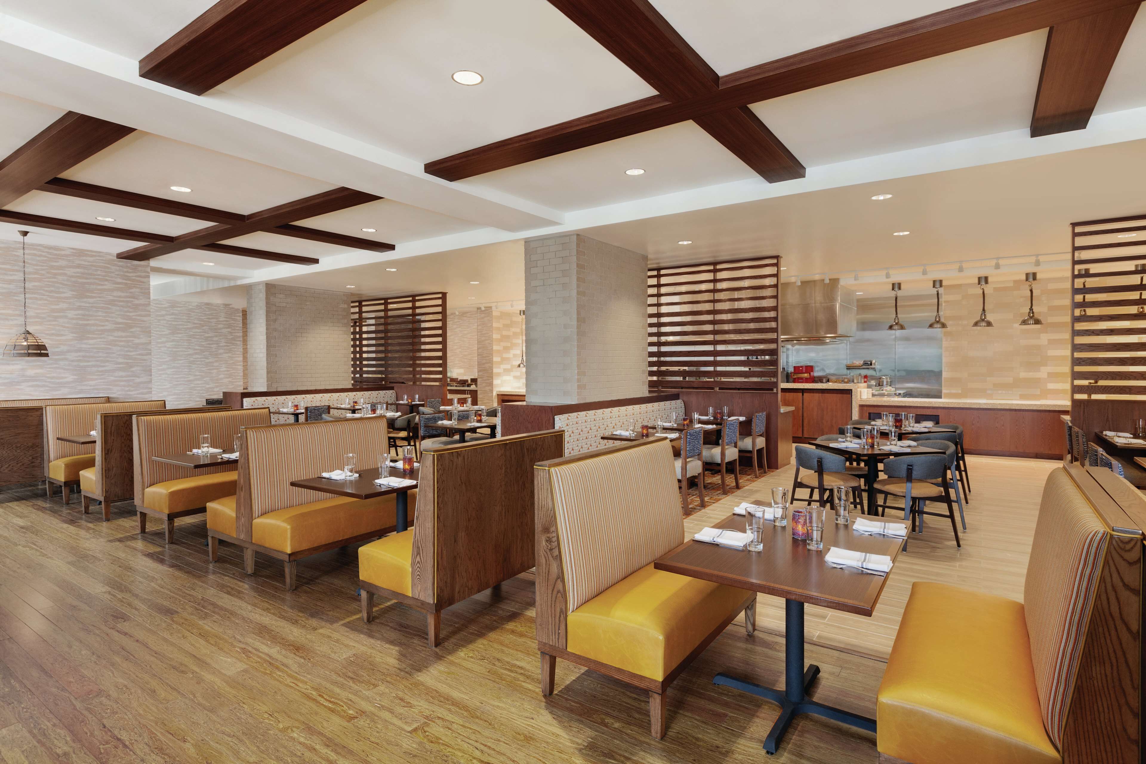 A modern restaurant with wooden beams, booths, and a central dining area.