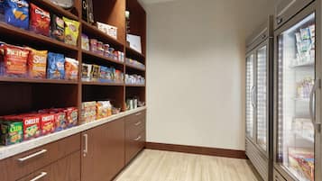 A pantry with shelves stocked with snacks and beverages, a clock, and a refrigerator.