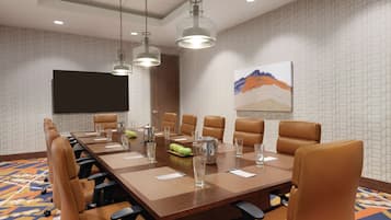 A conference room with a long table, brown leather chairs, and a flat-screen TV on the wall.