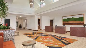 A spacious lobby with a large geometric patterned carpet, a reception desk, and a painting of a landscape on the wall.