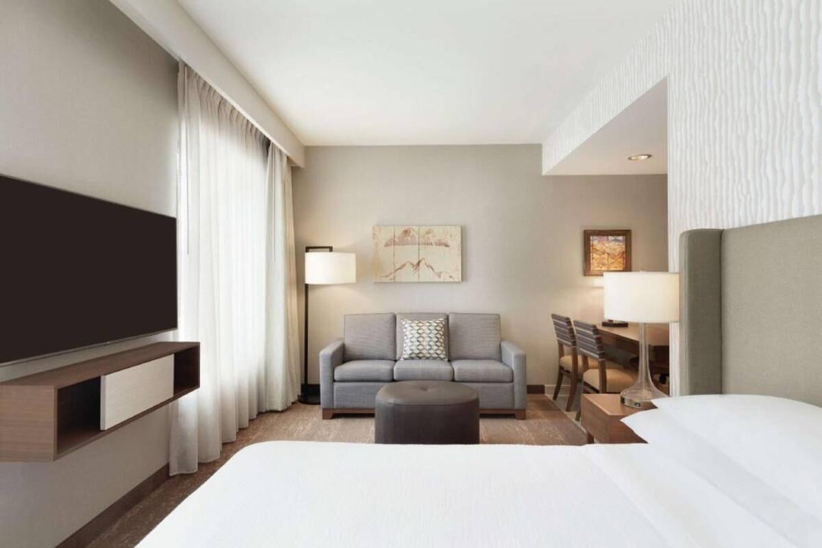 A hotel room with a bed, a sofa, a desk, and a TV.