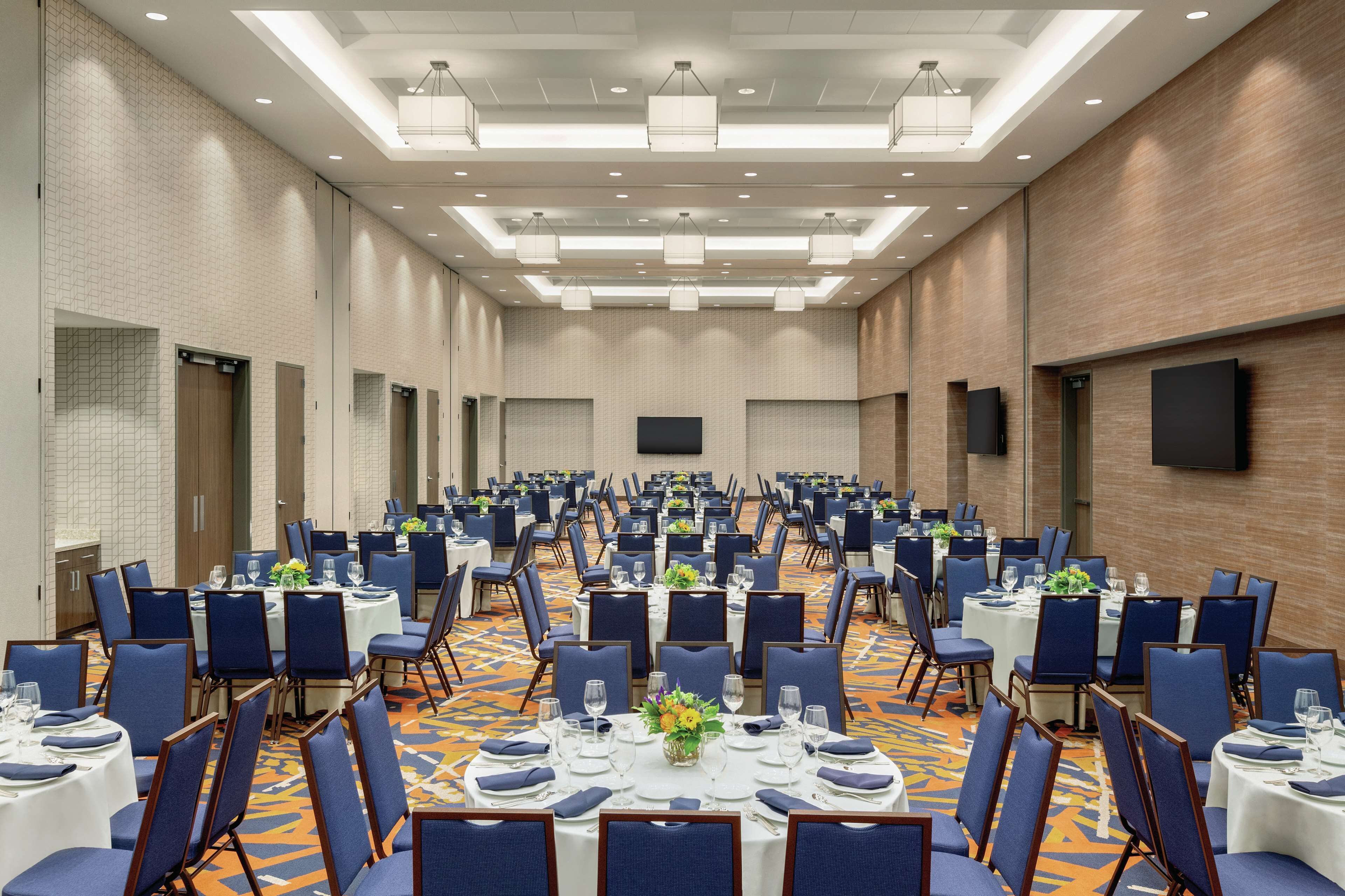 A large conference room with rows of tables and chairs, equipped with tables, chairs, and a flat-screen TV.