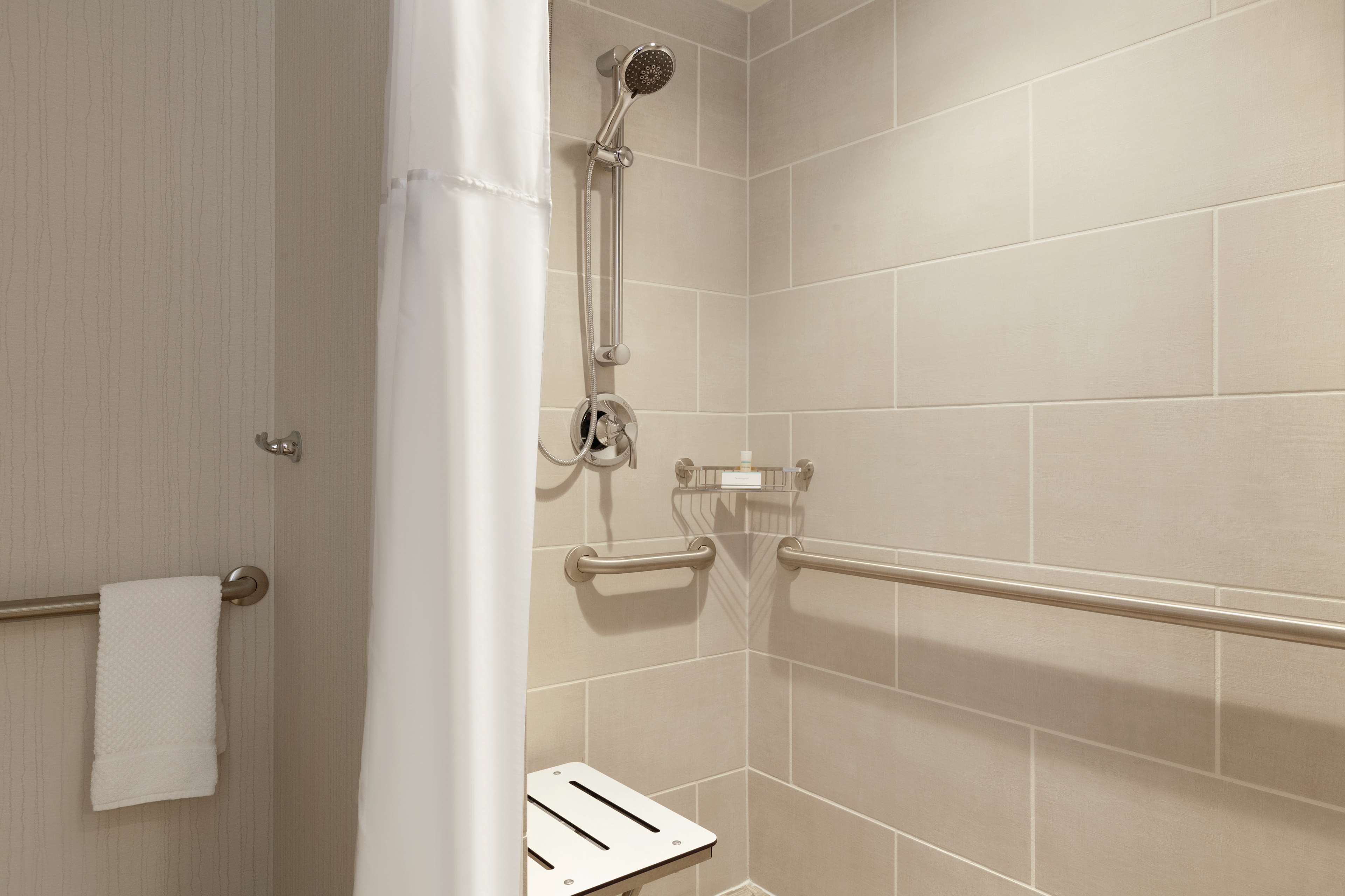 Un espace douche équipé d’un pommeau de douche à main, de barres d’appui et d’un porte-serviettes.