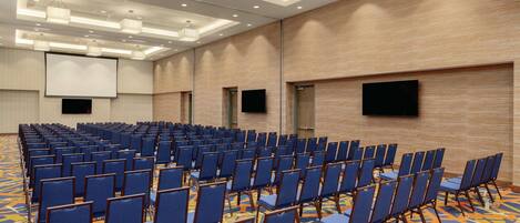 A conference room with rows of blue chairs, a large screen, and a patterned carpet.