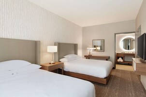 Una habitación de hotel con dos camas, un tocador con espejo y un televisor de pantalla plana.