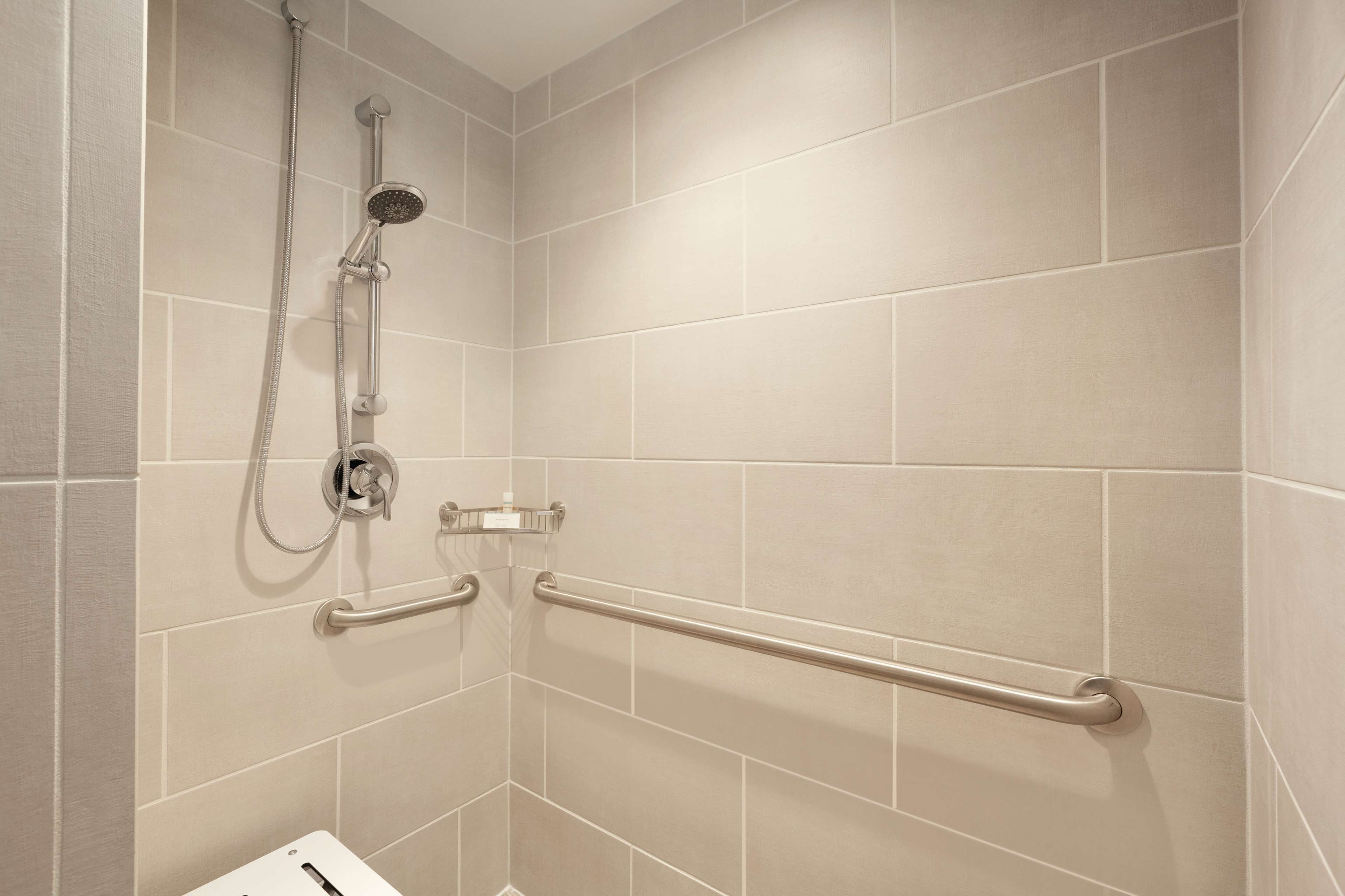 A shower area with beige tiles, a handheld showerhead, and a grab bar.