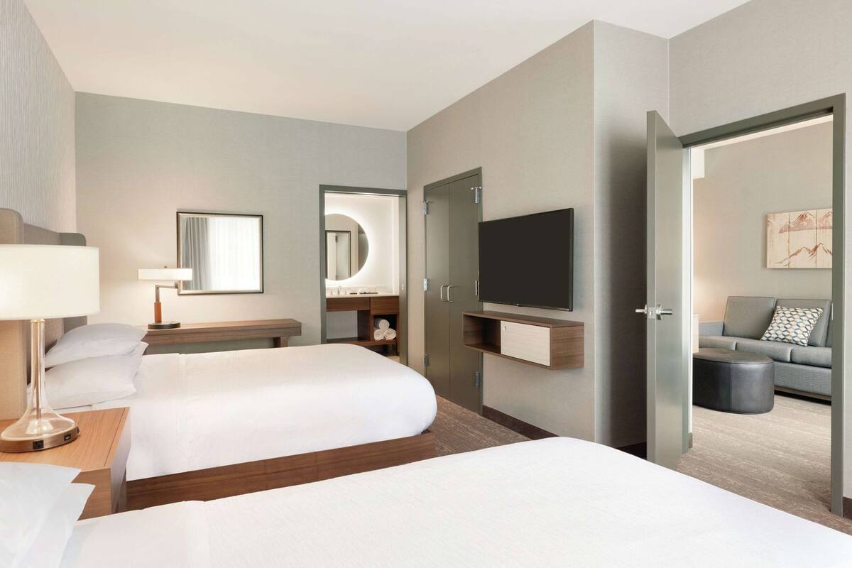 Une chambre d’hôtel avec deux lits, une télévision, un bureau, un miroir et un canapé.