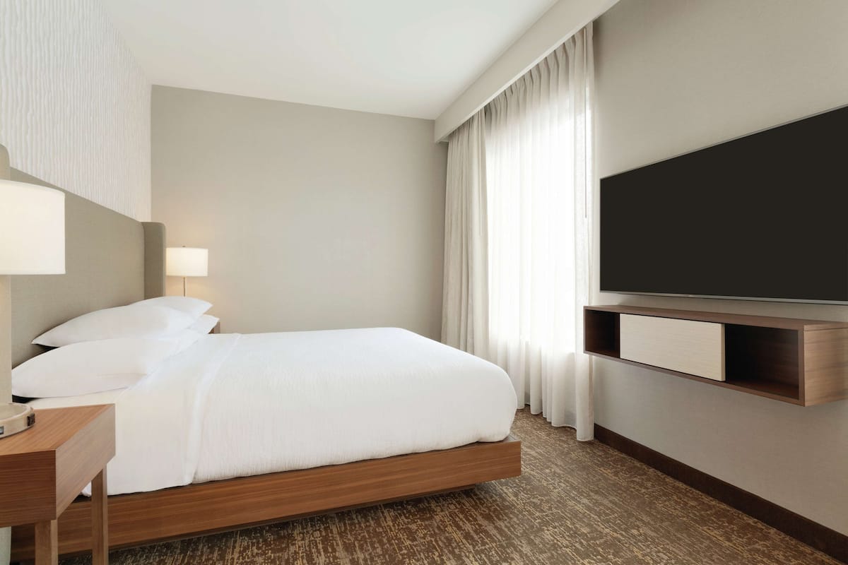 A hotel room with a bed, bedside table, lamp, TV, and curtains.