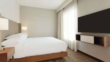 Quarto de hotel com cama, mesa de cabeceira, luminária, TV e cortinas.