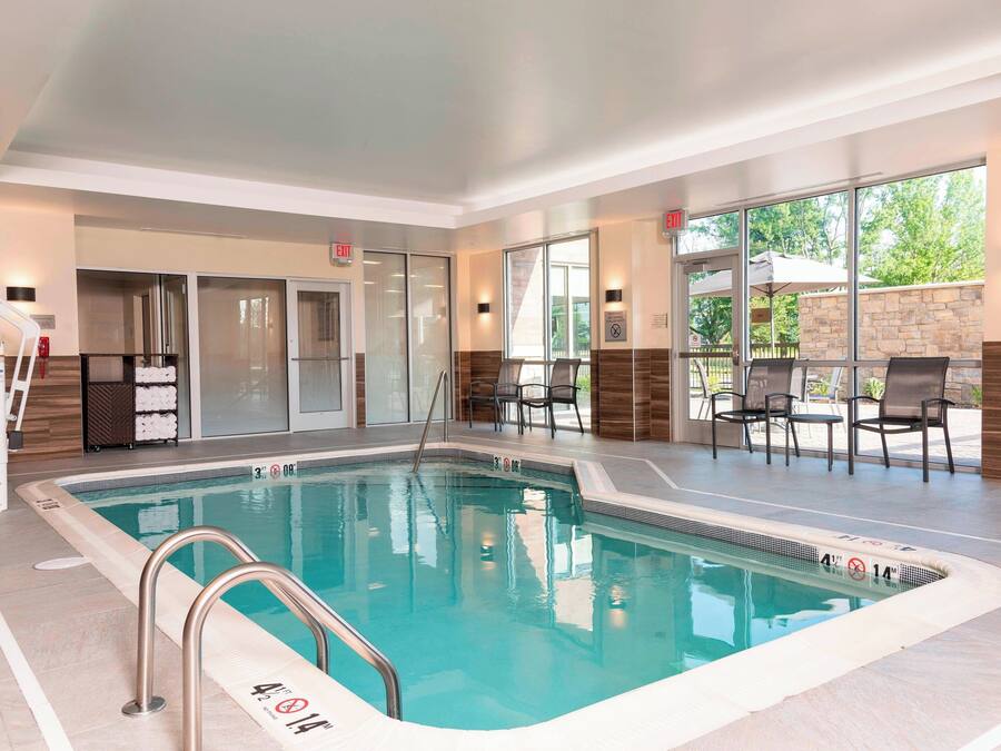 An indoor swimming pool with clear water, a lifeguard chair, and a set of stairs leading to a door.