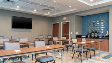 A conference room with multiple tables, chairs, a flat-screen TV, and a kitchen area with appliances.