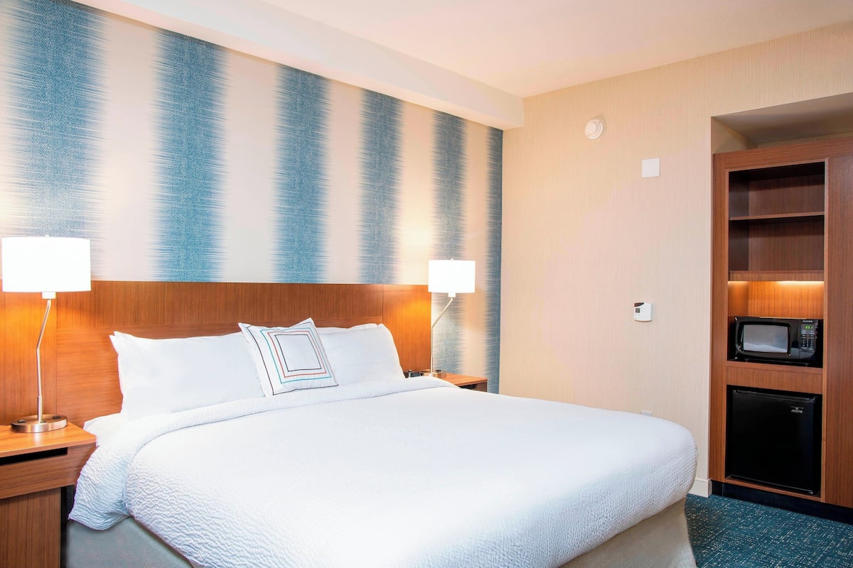Habitación de hotel con una cama grande, dos lámparas de noche, un microondas y un refrigerador.