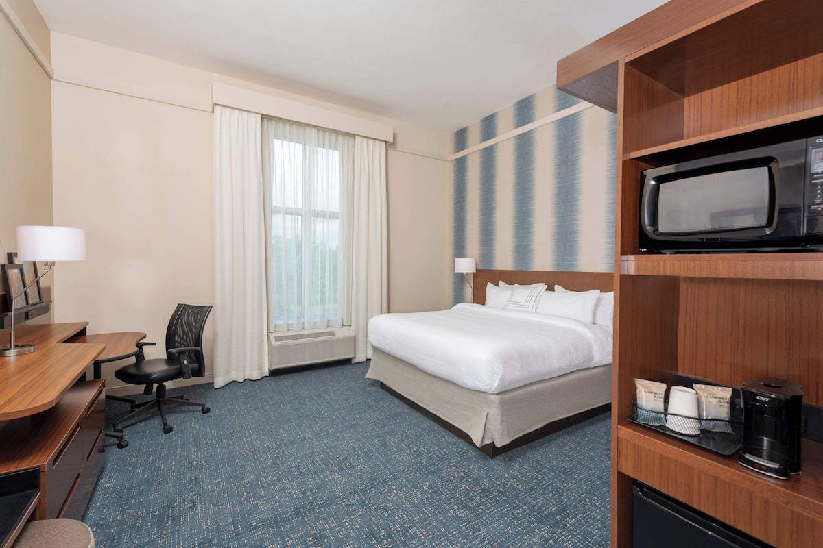 Habitación de hotel con cama, escritorio, silla y microondas en un estante.