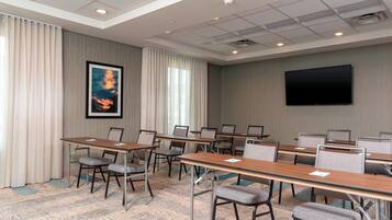 A conference room with multiple tables and chairs, a large flat-screen TV on the wall, and a patterned carpet.