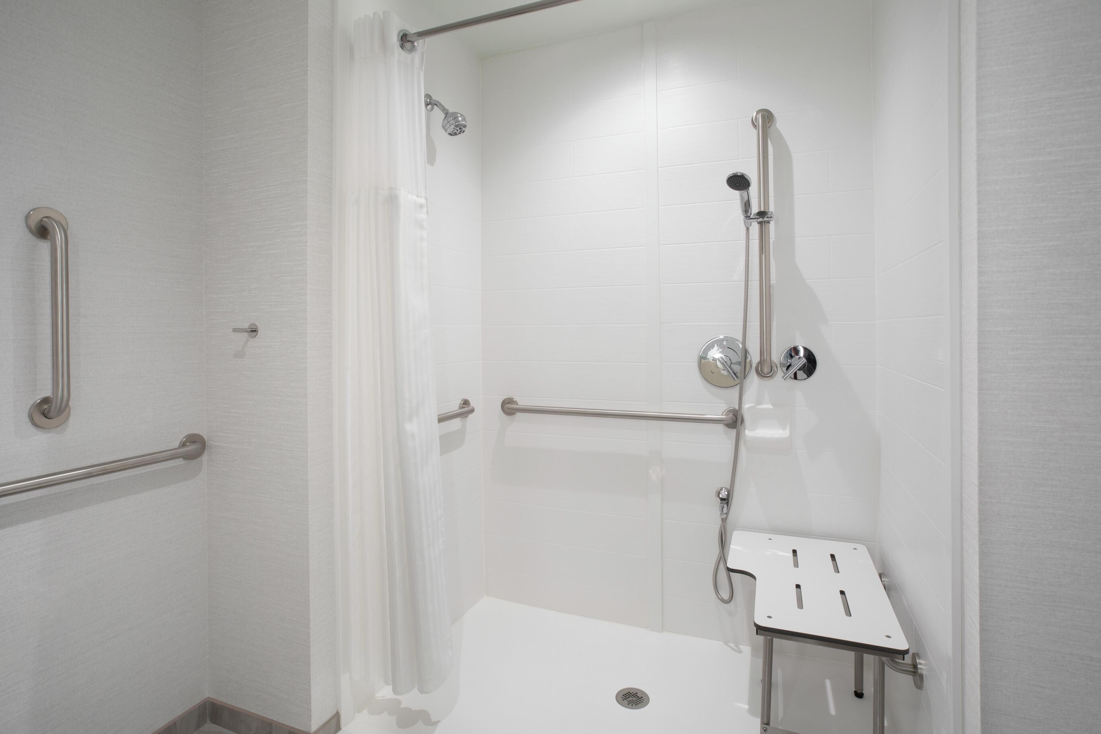 Une douche équipée d’une barre d’appui, d’un pommeau de douche à main et d’un siège.