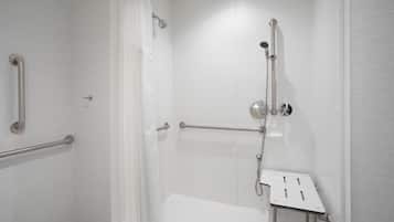 Une douche équipée d’une barre d’appui, d’un pommeau de douche à main et d’un siège.