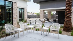 Une terrasse extérieure avec des meubles en osier blanc, des piliers en pierre et un palmier.