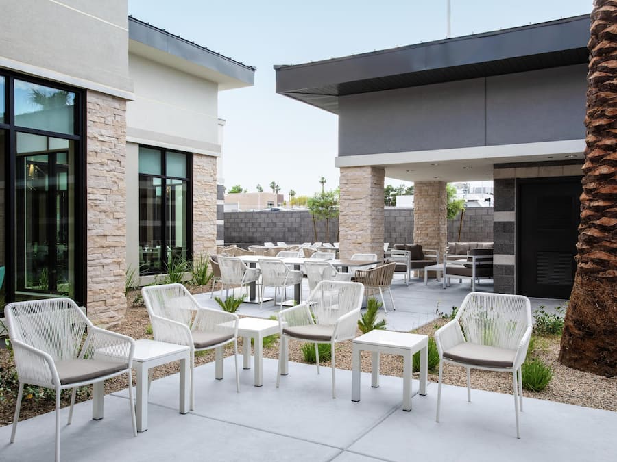 An outdoor patio with white wicker furniture, stone pillars, and a palm tree.