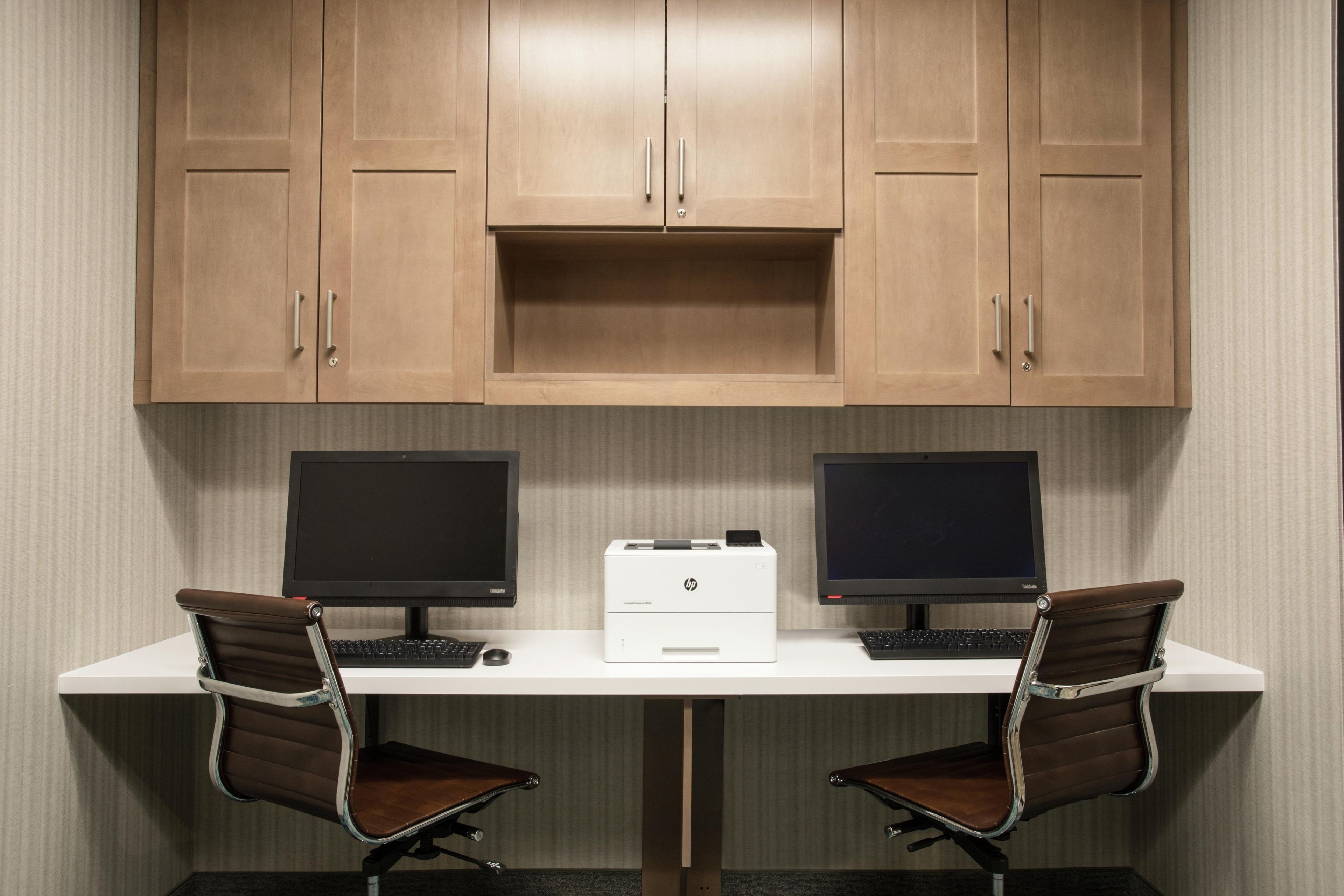 A workspace with two monitors, a printer, and two office chairs.