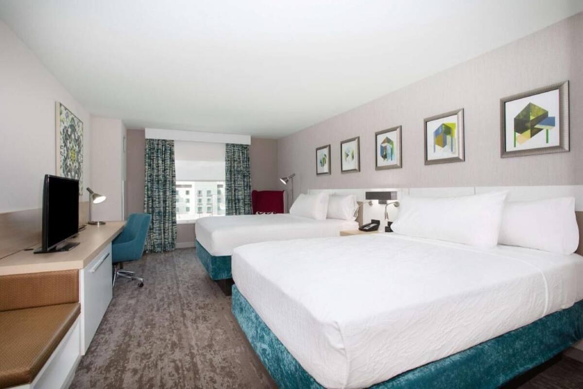A hotel room with two beds, a desk, a chair, a TV, and framed pictures on the wall.