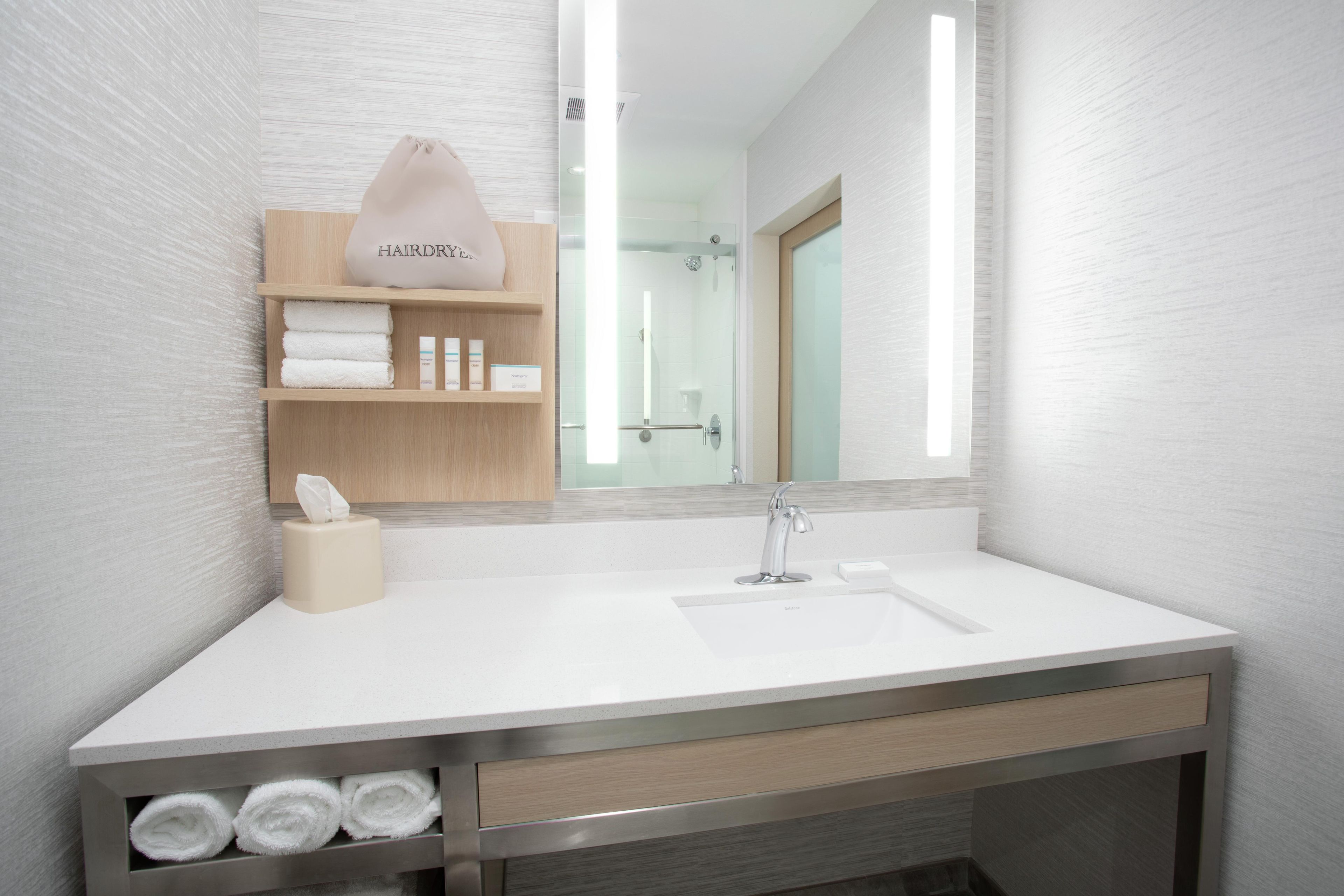 Une salle de bain moderne avec un lavabo blanc, un miroir, un porte-serviettes et une étagère de rangement.