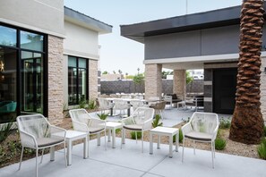 Un patio al aire libre con mobiliario de mimbre blanco, pilares de piedra y una palmera.